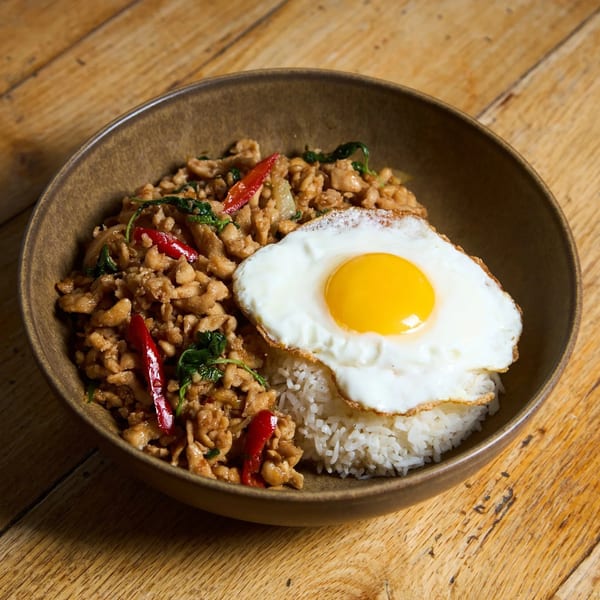 Thai basil chicken with red chilies, white rice, and a fried egg in a brown bowl.