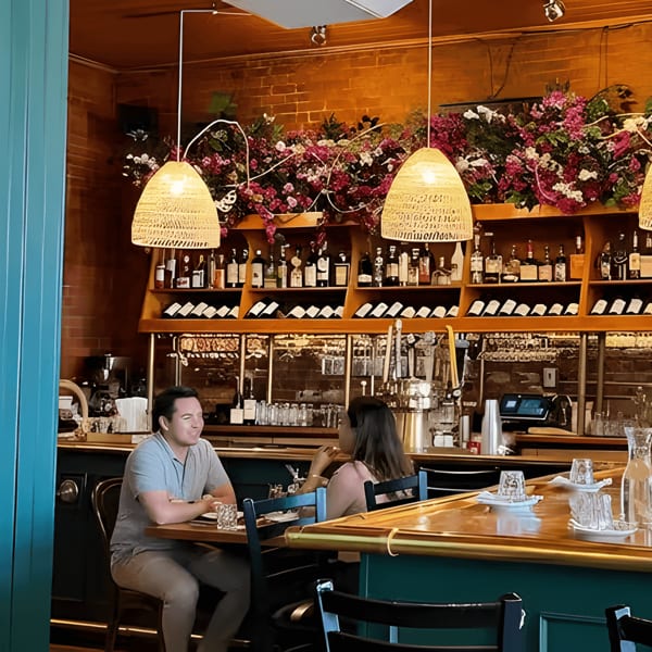 Two people seated at a bar with a full liquor and wine display behind them.