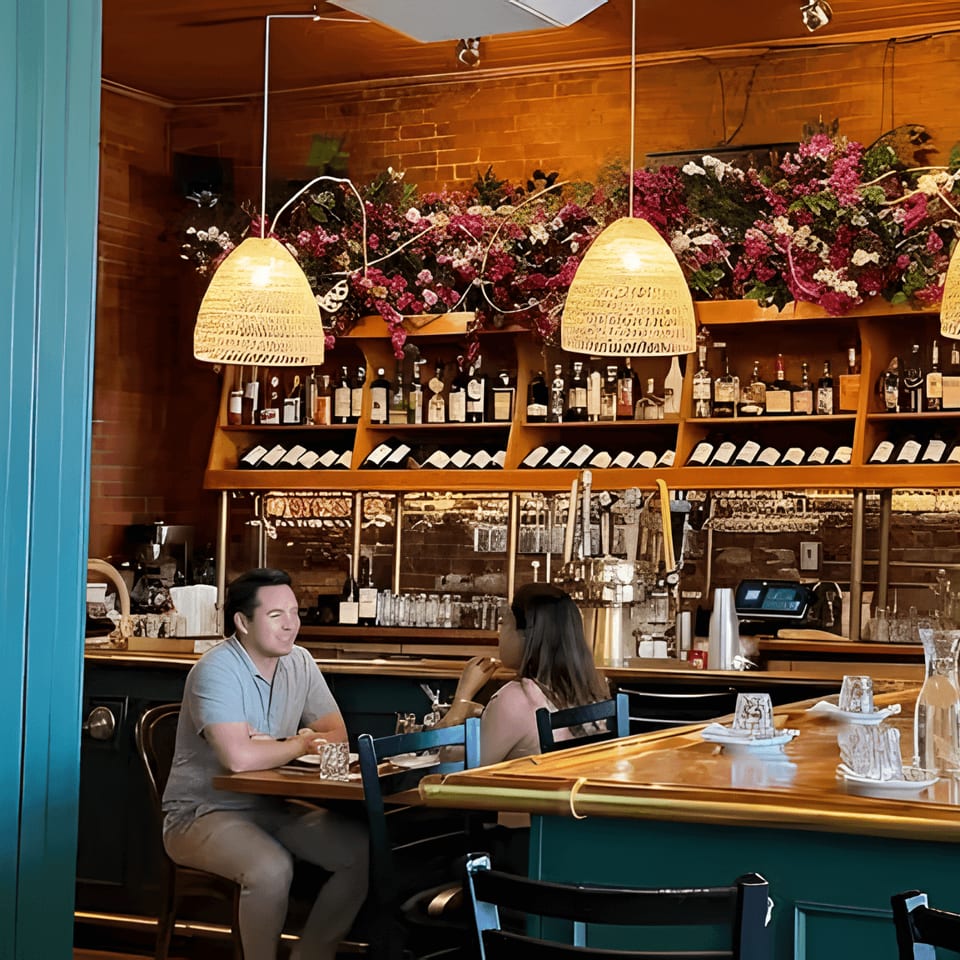Two people seated at a bar with a full liquor and wine display behind them.