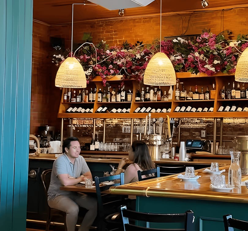 Two people seated at a bar with a full liquor and wine display behind them.