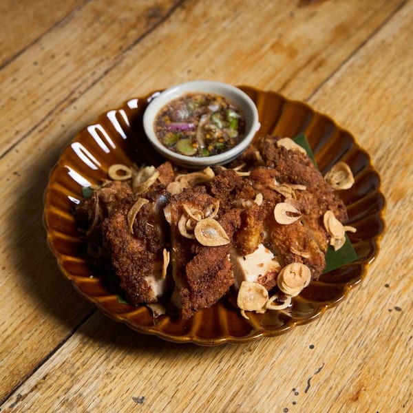 Crispy fried chicken pieces topped with fried garlic, served with a dipping sauce on a wooden table.