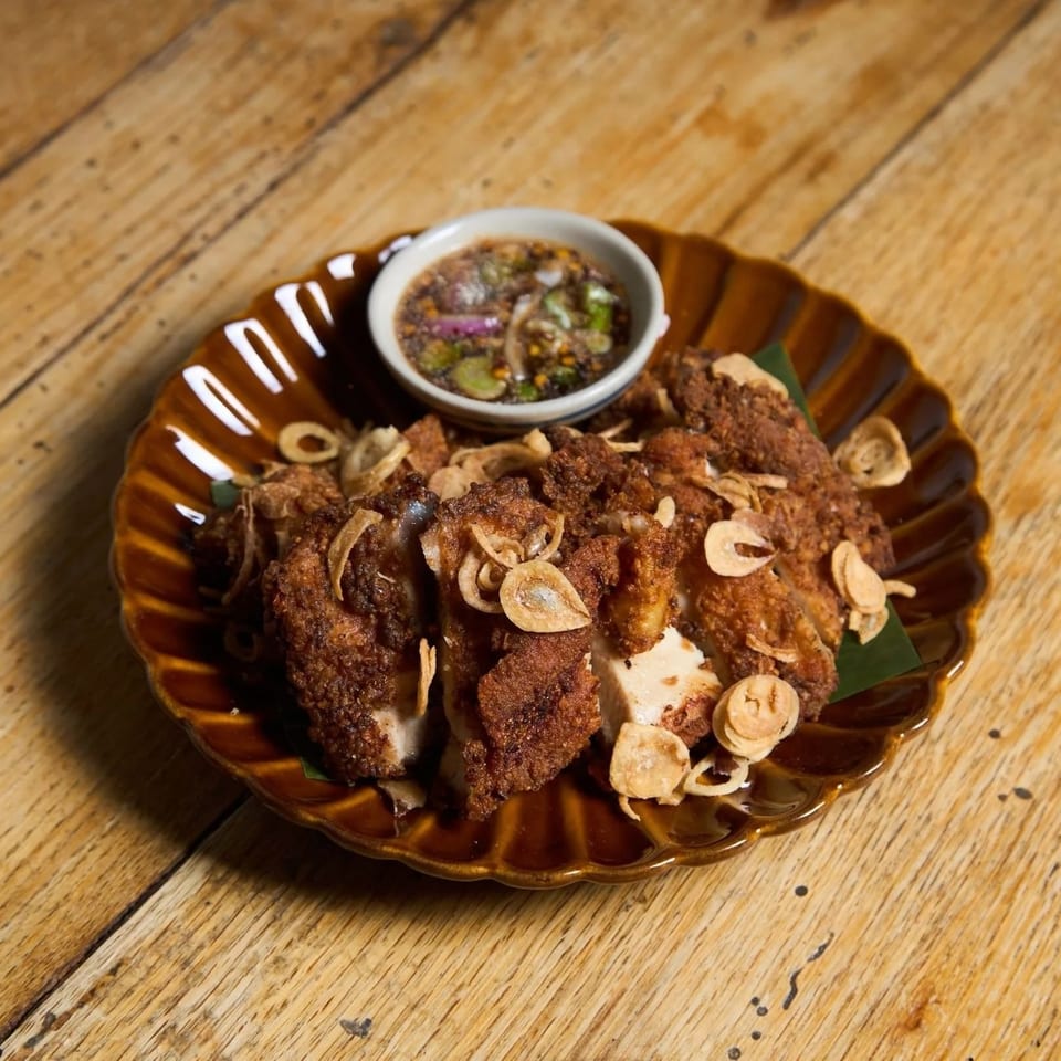 Crispy fried chicken pieces topped with fried garlic, served with a dipping sauce on a wooden table.