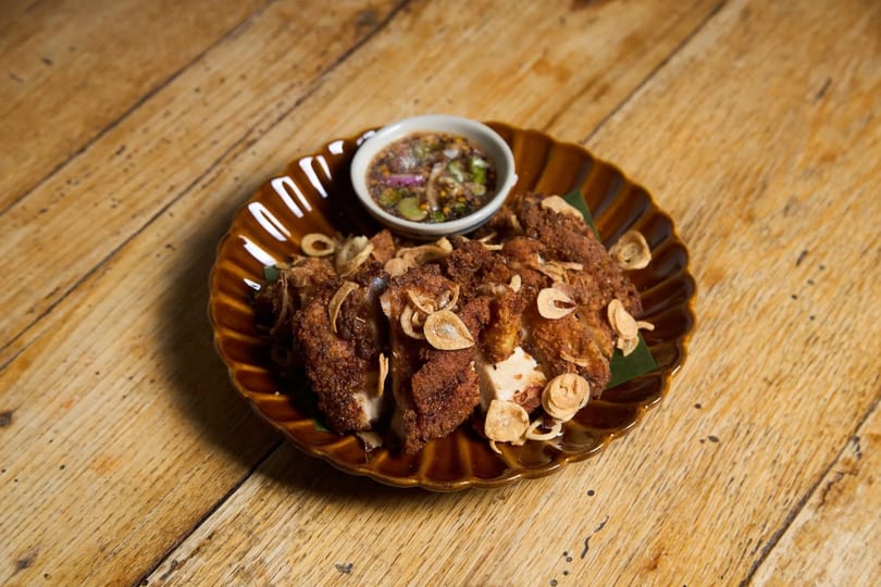 Crispy fried chicken pieces topped with fried garlic, served with a dipping sauce on a wooden table.