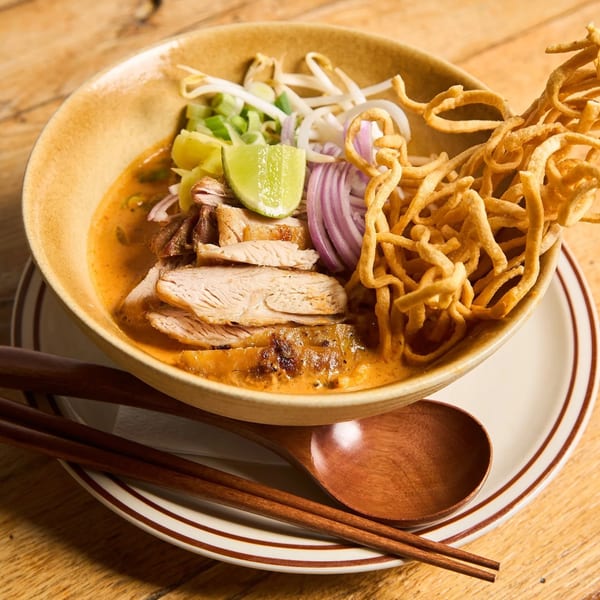 A bowl of Khao Soi with chicken, crispy noodles, red onion, lime, and bean sprouts.
