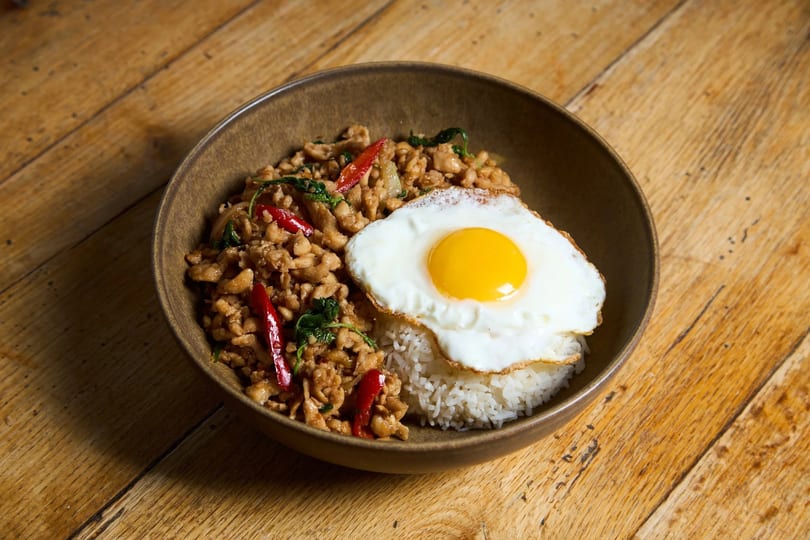 Thai basil chicken with red chilies, white rice, and a fried egg in a brown bowl.