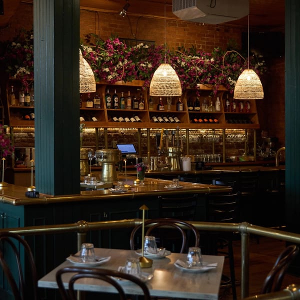 Cozy restaurant interior with a bar, wine shelves, hanging lights, and set tables with chairs.