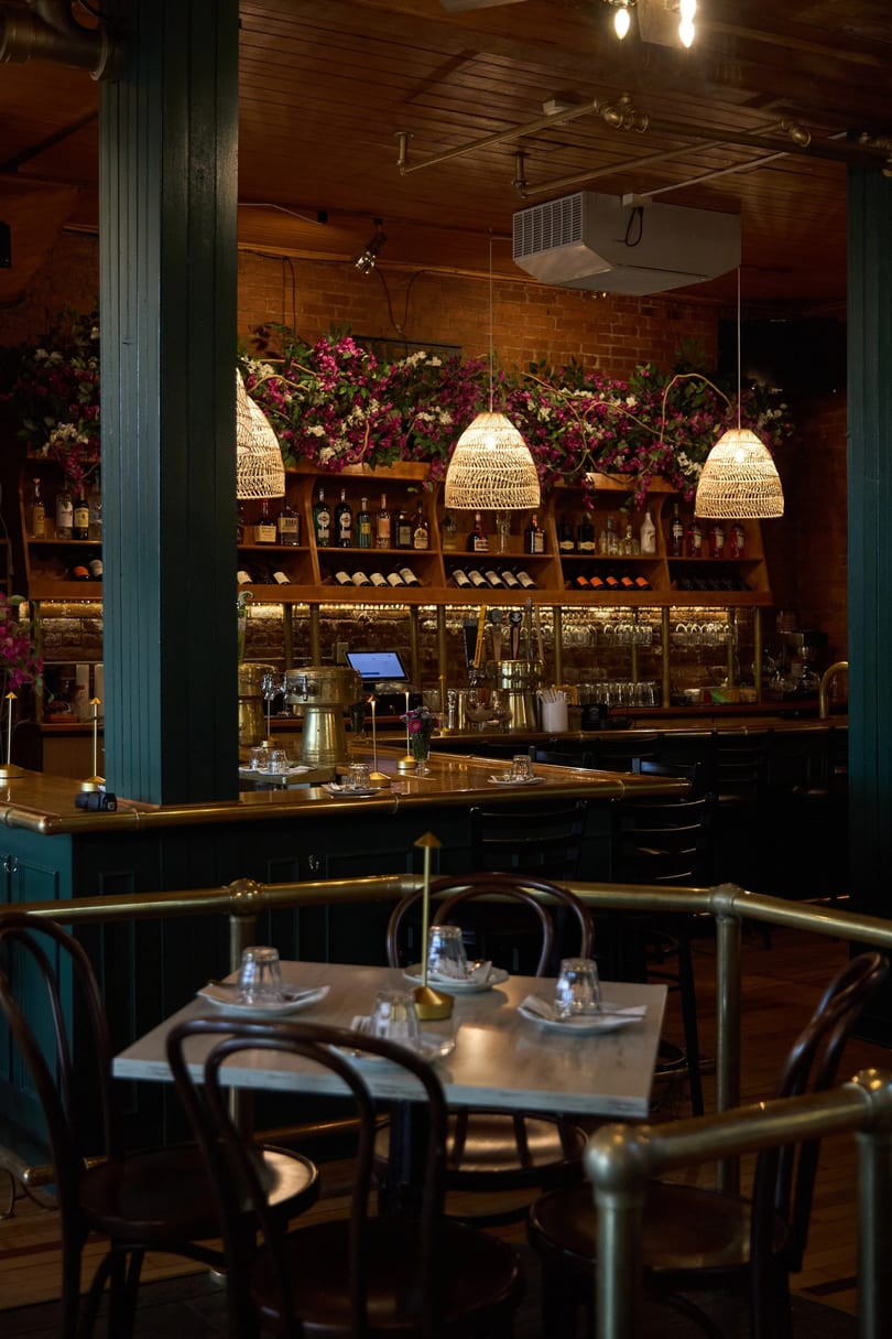 Cozy restaurant interior with a bar, wine shelves, hanging lights, and set tables with chairs.