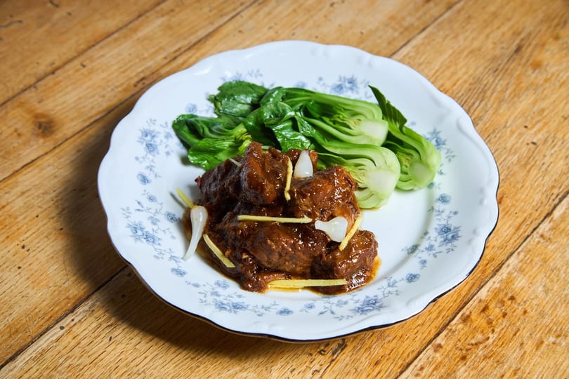 Braised beef with ginger, garlic, and bok choy on a white plate with blue floral patterns.