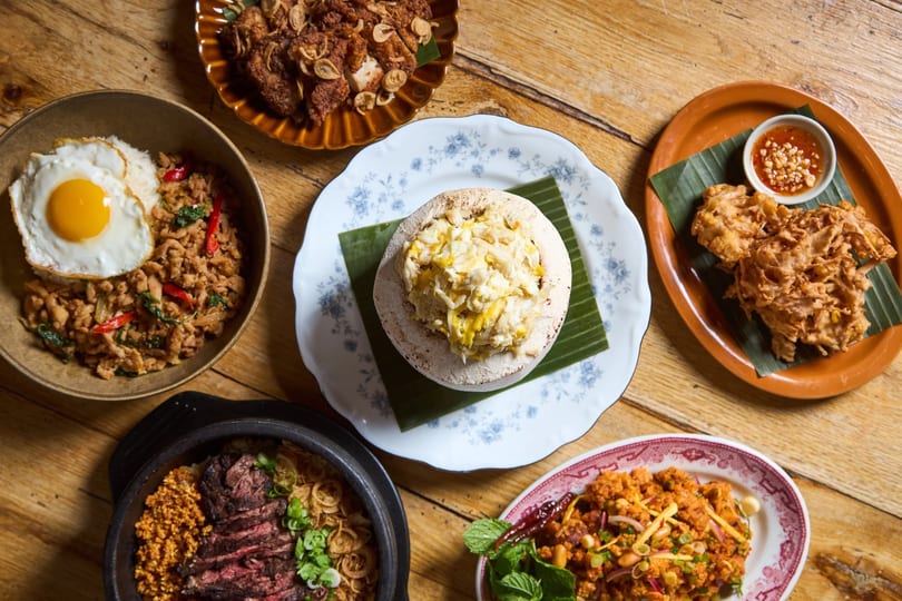 Overhead view of various Thai dishes, including fried chicken, rice with egg, and crab in a coconut.
