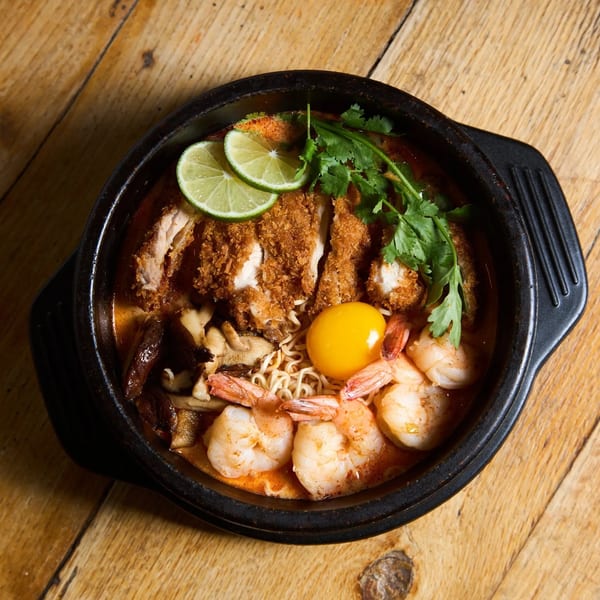 Top-down view of a ramen bowl with fried chicken, shrimp, lime, cilantro, and an egg yolk.