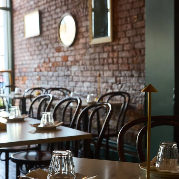 Restaurant interior with set tables, dark wooden chairs, and a brick wall adorned with mirrors.